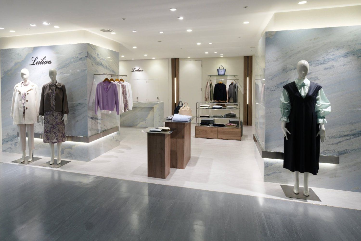 Womenswear boutique with large blue-grey stone volumes lit from below and wood-grain fixtures